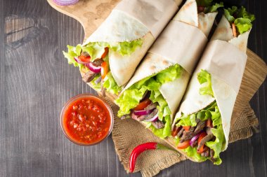 Fotoğraf Meksika sandviç gıda, börek, fajita, tacos, paket tortilla, sığır eti, tavuk, taze sebze rustik ahşap zemin üzerine yapılmış. Fast food kavramı. Sağlıklı yemek yemek. Kopya alanı. 