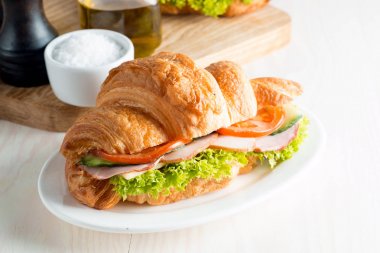 Taze kruvasan veya sandviç salata, jambon, jamon, jambon, salam, peynir, tavuk, domates ahşap arka plan ile. Sabah kahvaltı kavramı. Sağlıklı ve fast food.