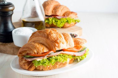 Taze kruvasan veya sandviç salata, jambon, jamon, jambon, salam, peynir, tavuk, domates ahşap arka plan ile. Sabah kahvaltı kavramı. Sağlıklı ve fast food.