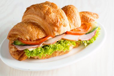 Taze kruvasan veya sandviç salata, jambon, jamon, jambon, salam, peynir, tavuk, domates ahşap arka plan ile. Sabah kahvaltı kavramı. Sağlıklı ve fast food.