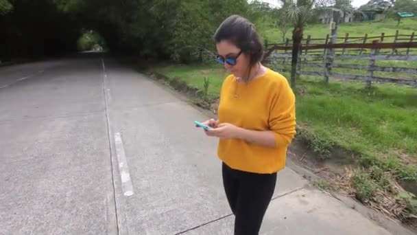 ストップ中に彼女の携帯電話上の情報を探している黄色のセーターの若い女性 広い角度 — ストック動画