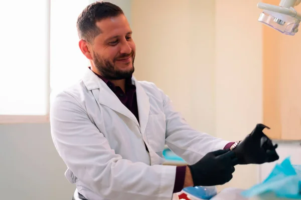 Latino dentist, wearing black diagnostic gloves, smile on his face