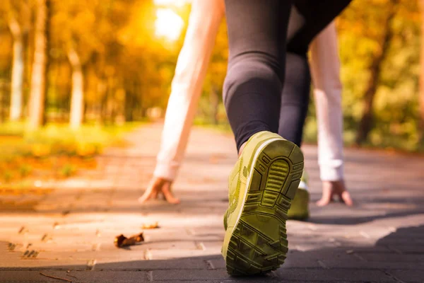 Athlete woman in running start pose on the city autumn park. Spo