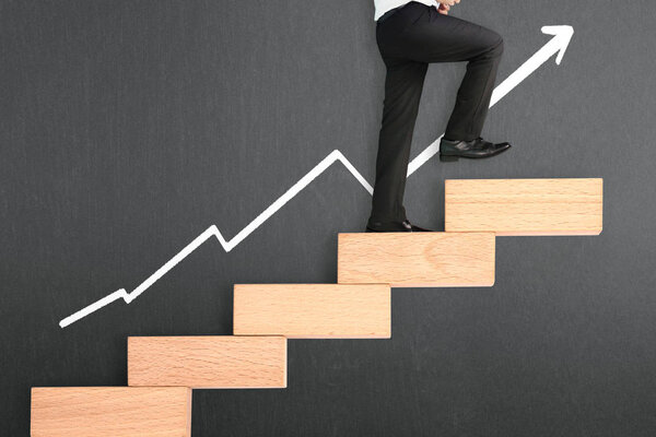 бизнесмен поднимается по игрушечной лестнице
