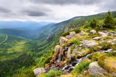 Beautiful waterfall above a deep green valley with mountains clipart