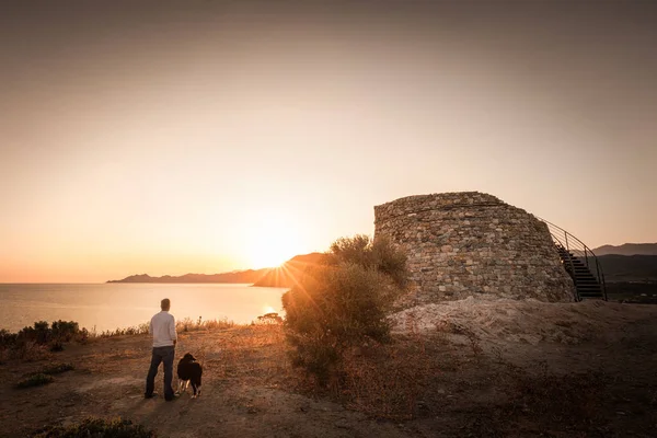 Man & dog watching Sunrise behind Genoese tower in Corsica — Stock Photo, Image