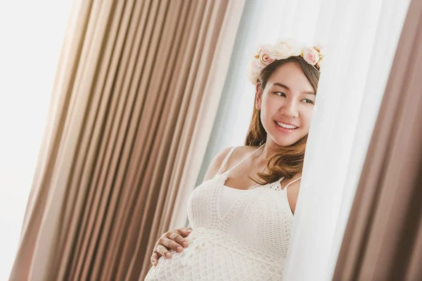 Jovem asiático grávida mulher de pé perto janela em casa. — Fotografia de Stock