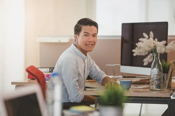 Νεαρός επιχειρηματίας χαμογελώντας ενώ κάθεται στον τόπο εργασίας στο γραφείο. — Φωτογραφία Αρχείου