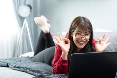 Genç Asyalı kadın evden tablet bilgisayarda çalışıyor, hafta sonunun keyfini çıkarıyor, ev konseptinden çalışıyor.