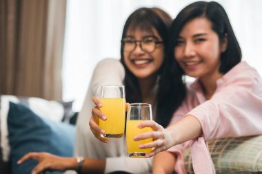 İki Asyalı kadın oturma odasında portakal suyu içiyor, ergen ya da arkadaş aktivitesi, bekarlık, kutlama konsepti..