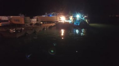 Balıkçı gemilerinden kargo kamyonlarına yükleme. Limandaki gemilerin ışıkları altında çalışan balıkçılar. Balıkçılık endüstrisi için ideal, gece işi hayatı. İşçiler gece yarısı liman limanında hareket edebilirler. Deniz piyadesi okyanus havası limanına demir atmışlardır..