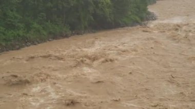 Hızlı akan azgın nehir. Toprak ve çamur aşağı doğru ilerliyor. Şiddetli yağmurdan sonra. Dev kaynamış kahverengi çamurlu su. Köpüklü akarsu tehlikeli bir dere. Kaynar su yaratıyor. Çevresel hasar.