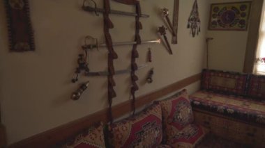 Ortadoğu 'daki evin duvarında silahlar asılı. Doğulu bir evin geleneksel mimarisi. Ana yaşam alanı. Tabanca tabancası, tabanca, tüfek, tüfek, silah, kılıç, claymore, 4k.