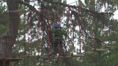 Çocuk macera parkında halat köprüsünü geçer. Macera parkı çok çeşitli elementleri barındıran ip köprüsünü geçebilen bir yerdir. Çocuk, yağmur ormanlarında mavi kasklı kırmızı ipler kullanıyor. 3840x2160 4K