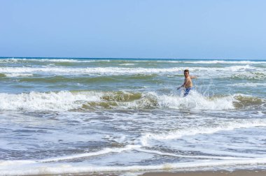 Çocuk sahilde bir gün geçirip deniz suyuyla oynuyor.