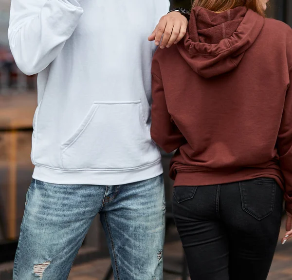 young couple wearing hoodie. man has white hoodie. girl has brown hoodie