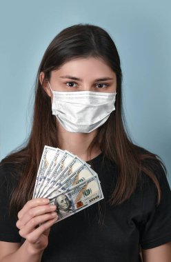 Yüz maskeli kadın kameraya bakarken Coronavirus covid 19 sırasında harçlık alıyor. Kızın elinde dolar banknotları var. İnsanların tazminatı. Kriz sırasında hükümet kapsamı