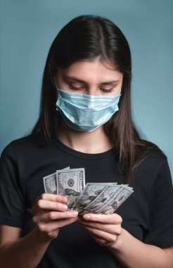 Yüz maskeli kadın, Coronavirus covid 19 sırasında harçlık alıyor. Kız elinde dolar banknotları tutuyor. İnsanların tazminatı. Kriz sırasında hükümet kapsamı