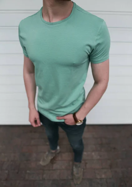 白いガレージのドアを背景に若い筋肉質の男の屋外で空のスリムな緑のTシャツのモックアップ — ストック写真