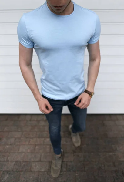 白いガレージのドアを背景に若い筋肉質の男の屋外で空のスリムブルーTシャツのモックアップ — ストック写真