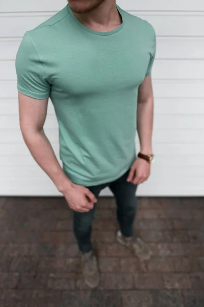 白いガレージのドアを背景に若い筋肉質の男の屋外で空のスリムな緑のTシャツのモックアップ — ストック写真