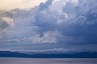 Gölün üzerinde dramatik bulutlar ve alacakaranlıkta dağlar.
