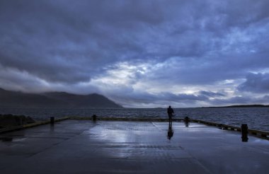 A person standing at Gledivik Bay looking at the dramatic stormy sky ahead, Djupivogur Village, East-Iceland clipart