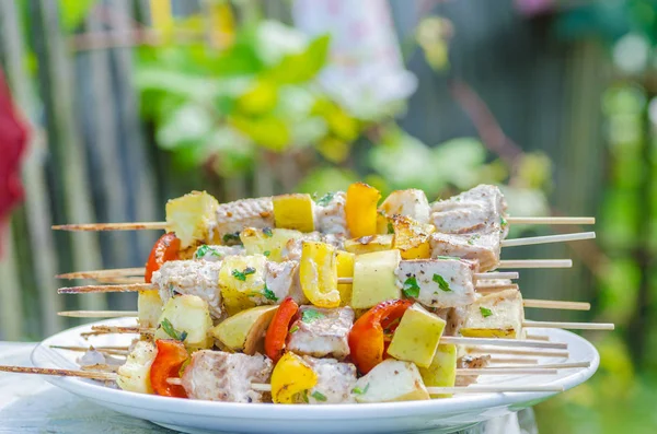 Espetos saborosos de peixe fresco com legumes e maçãs em um prato de carne shish de madeira Imagem De Stock