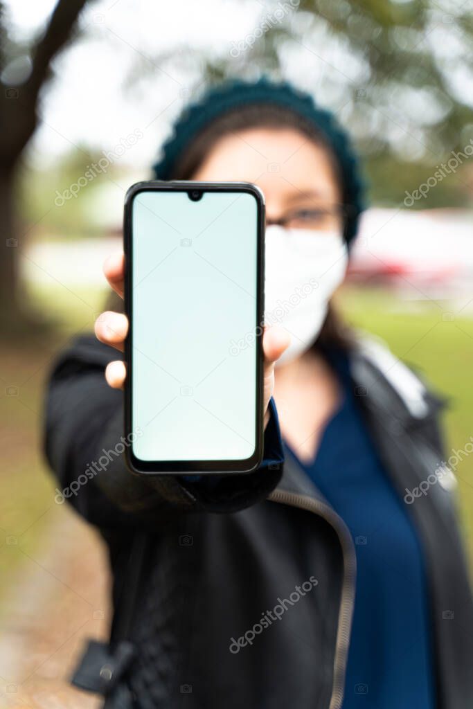woman with mask looks at her cell phone on the street