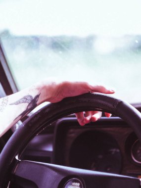 Avrupa 'da eski bir arabanın direksiyonuna dövmeli bir erkek eli yakın çekimde, direksiyon solda.