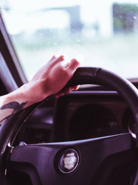 Avrupa 'da eski bir arabanın direksiyonuna dövmeli bir erkek eli yakın çekimde, direksiyon solda.