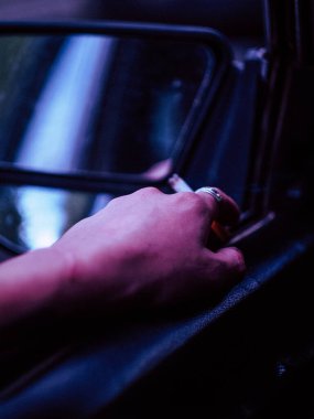 Genç dövmeli bir adamın direksiyonda oturup eski bir araba sürüşünün arka görüntüsü.