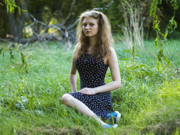 Bella ragazza bionda seduta su erba verde in un parco cittadino — Foto Stock