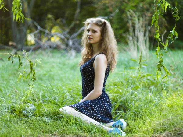 Linda menina loira sentada na grama verde em um parque da cidade — Fotografia de Stock