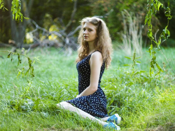 Hermosa chica rubia sentada sobre hierba verde en un parque de la ciudad — Foto de Stock