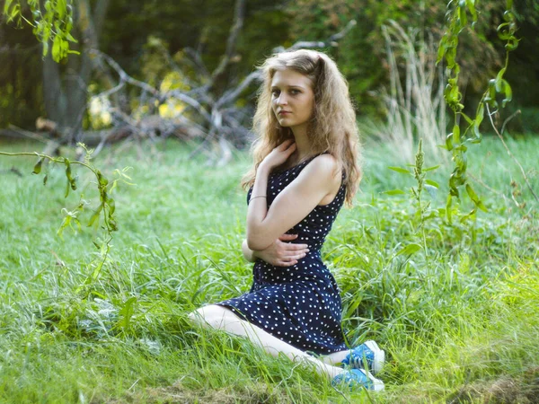 Bella ragazza bionda seduta su erba verde in un parco cittadino — Foto Stock