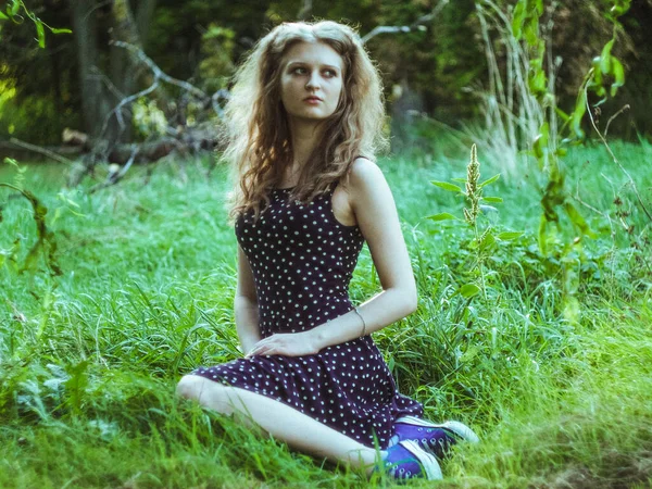 Linda menina loira sentada na grama verde em um parque da cidade — Fotografia de Stock