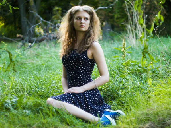 Bella ragazza bionda seduta su erba verde in un parco cittadino — Foto Stock