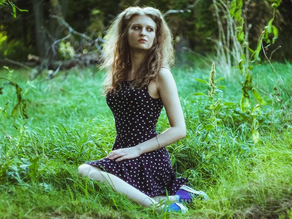 Krásná blondýnka dívka sedí na zelené trávě v městském parku — Stock fotografie
