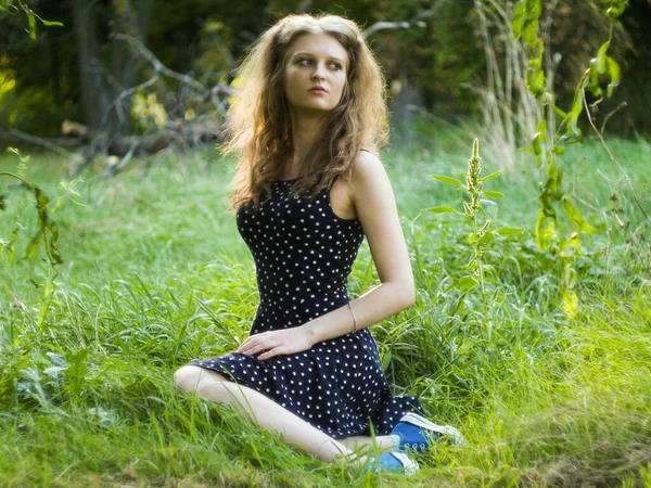 Bella ragazza bionda seduta su erba verde in un parco cittadino — Foto Stock