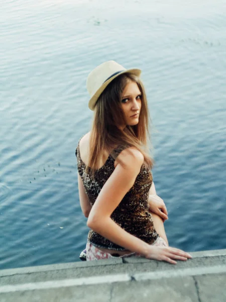 美丽的Boho女孩站在日落附近湖边 身穿白色波希米亚服装 头戴风帽 头戴草帽的年轻貌美女子 在绿叶中轻松自在地呆在水边 — 图库照片