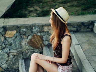 Gün batımında göl kenarında duran güzel boho kızı. Beyaz bohem elbiseli, rüzgarlı saçlı, yeşil yaprakların arasında, suyun yanında dinlenen hasır şapkalı çekici genç bir kadın. yaz tatili