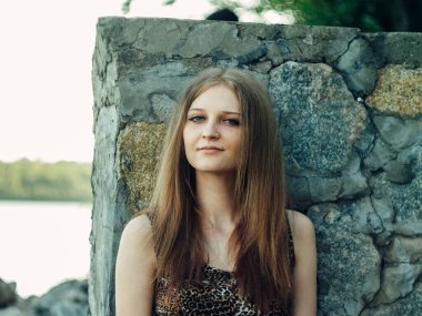 Gün batımında göl kenarında duran güzel boho kızı. Beyaz bohem elbiseli, rüzgarlı saçlı, yeşil yaprakların arasında, suyun yanında dinlenen hasır şapkalı çekici genç bir kadın. yaz tatili