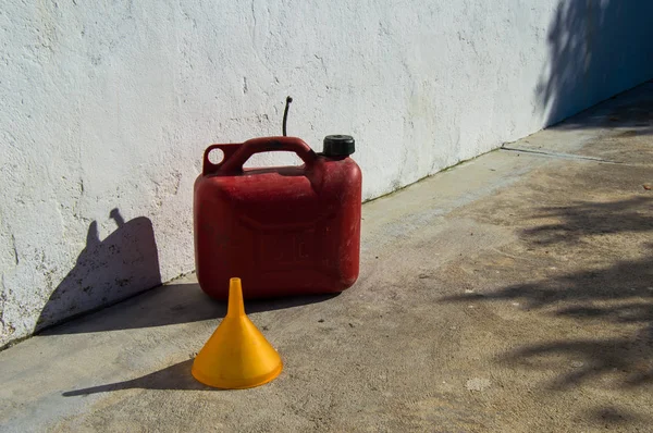 Red gasoline jerrycan of five liter and a yellow funnel. Outdoors views of a rural place during a sunny day