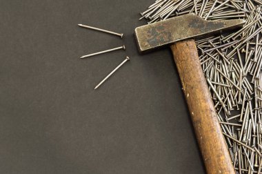 Farklı metal çivi yığınları ve siyah zemin üzerinde eski bir çekiç ve sol tarafında da fotokopi alanı. Marangozluk kavramına sahip koyu arkaplan.