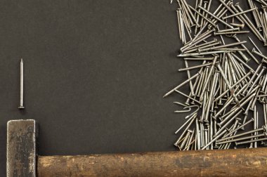 Farklı metal çivi yığınları ve siyah zemin üzerinde eski bir çekiç ve sol tarafında da fotokopi alanı. Marangozluk kavramına sahip koyu arkaplan.