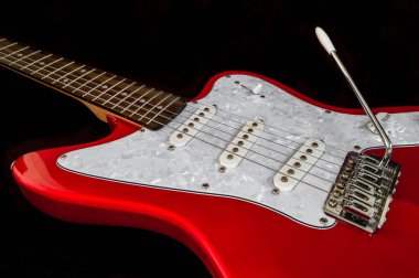 Siyah arka planda izole edilmiş güzel kırmızı elektro gitar. Vibrato çubuğu ve ses düğmesi olan müzik aleti, detaylarla kapat.