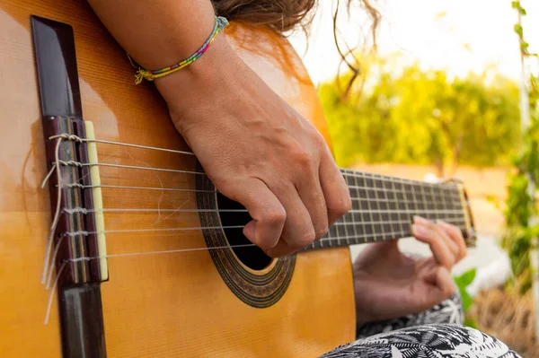 Young woman playing a spanish or classical guitar sitting in a field on a sunny day. Close up music lifestyle.