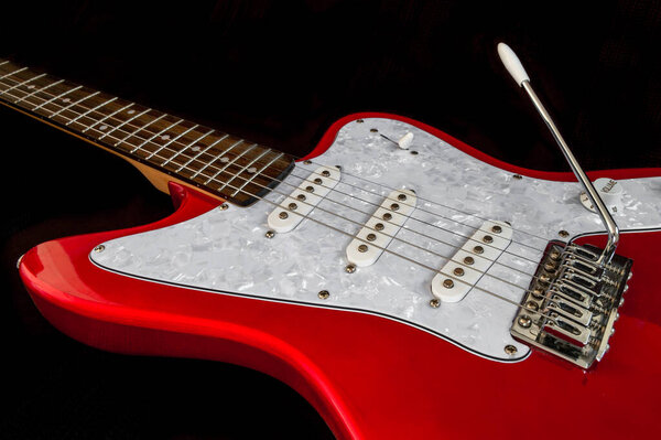 Beautiful red electric guitar isolated on black background. String musical instrument with vibrato bar and volume button, close up with details.