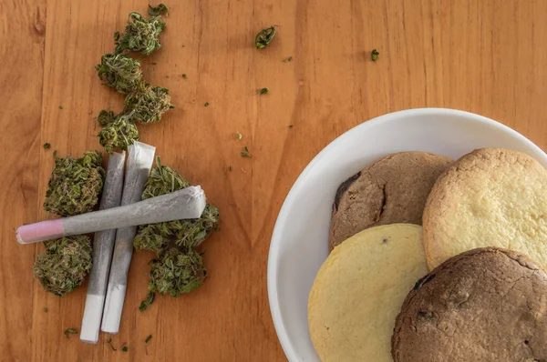 Sarılmış esrar tomurcukları ve ahşap masada ev yapımı marihuana kurabiyeleri. Ot ve kurabiye kahvaltısı..